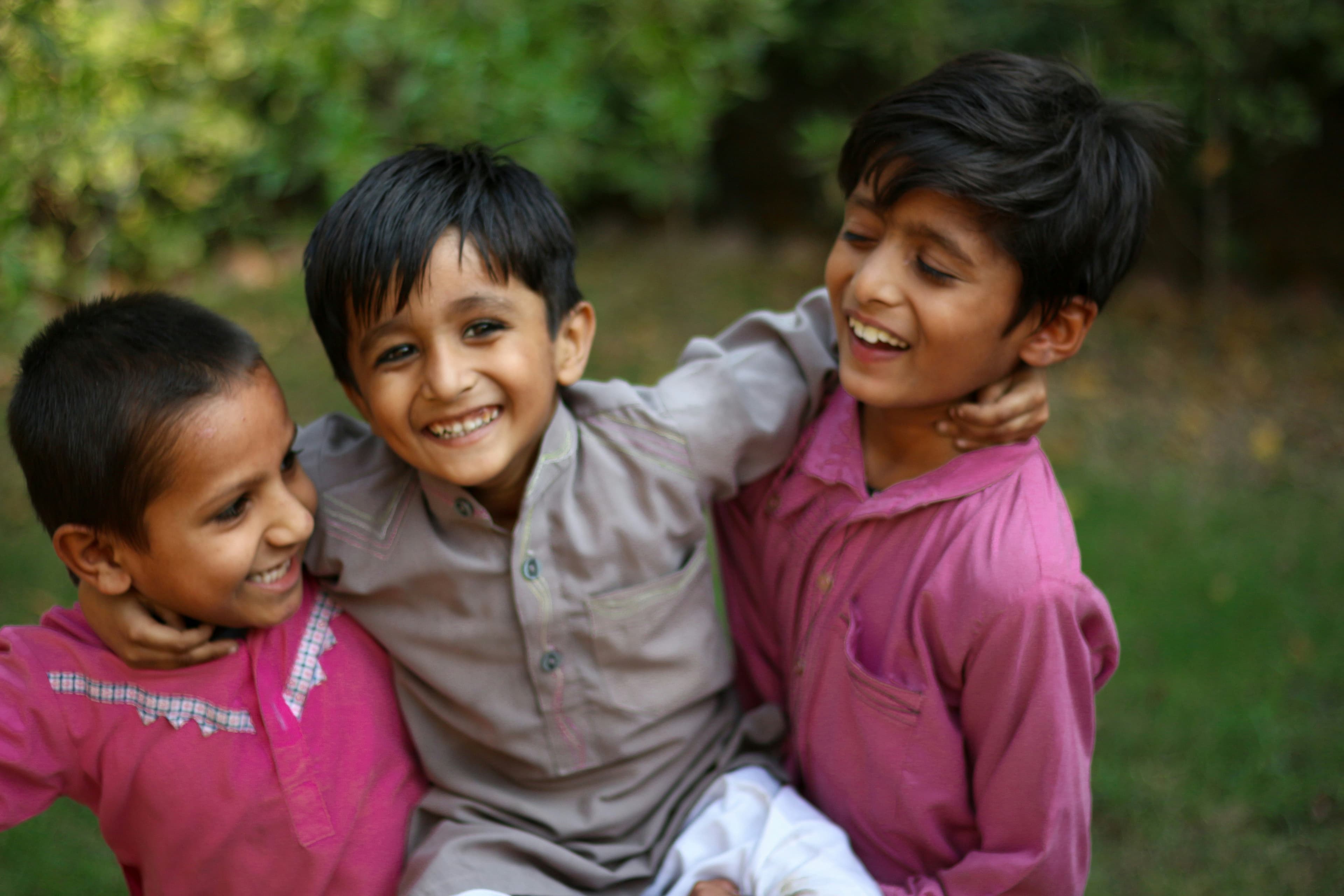 Three young brothers laughing with their arms around each other.