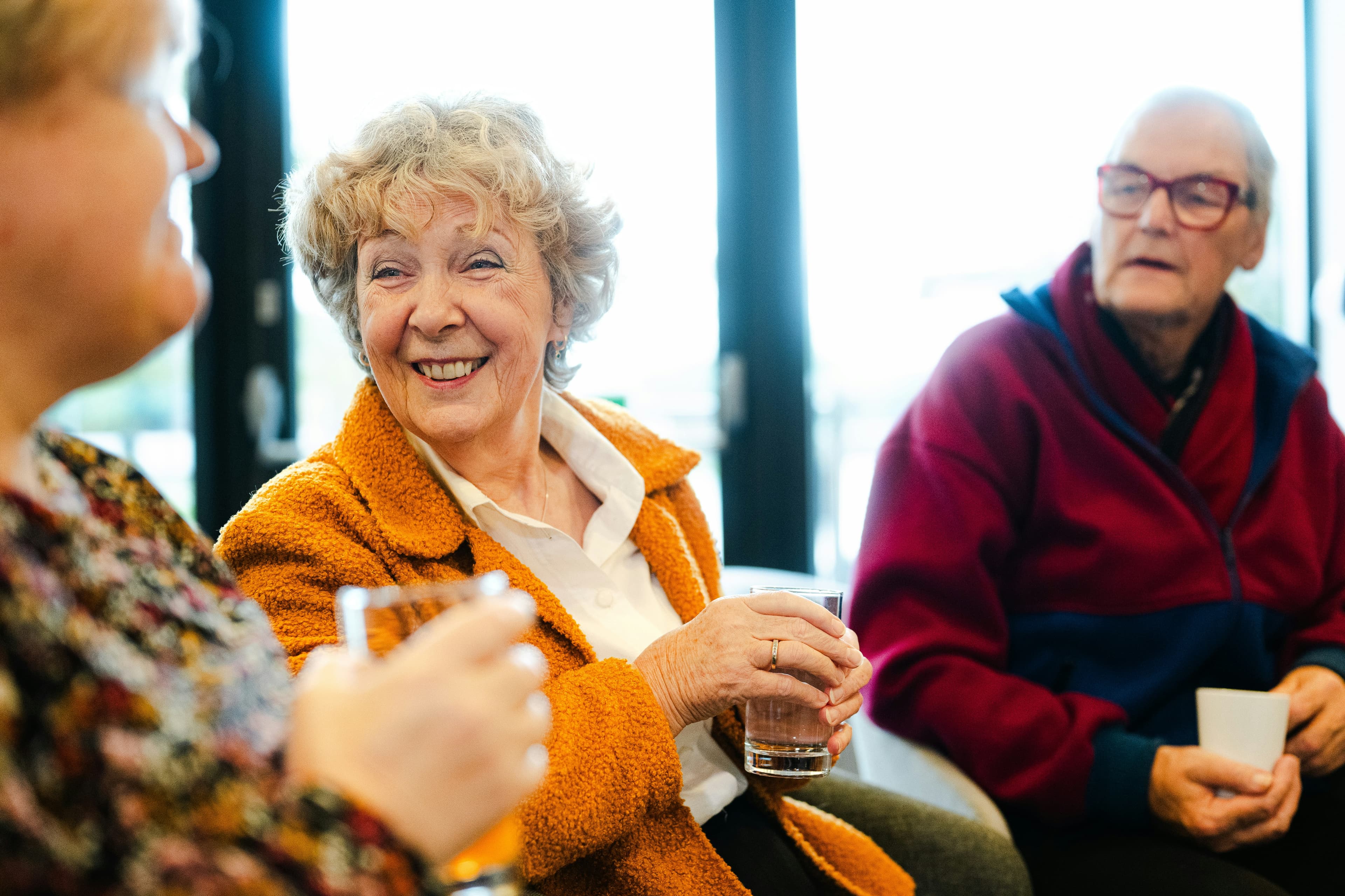 An older woman laughing with friends over a glass of water.
