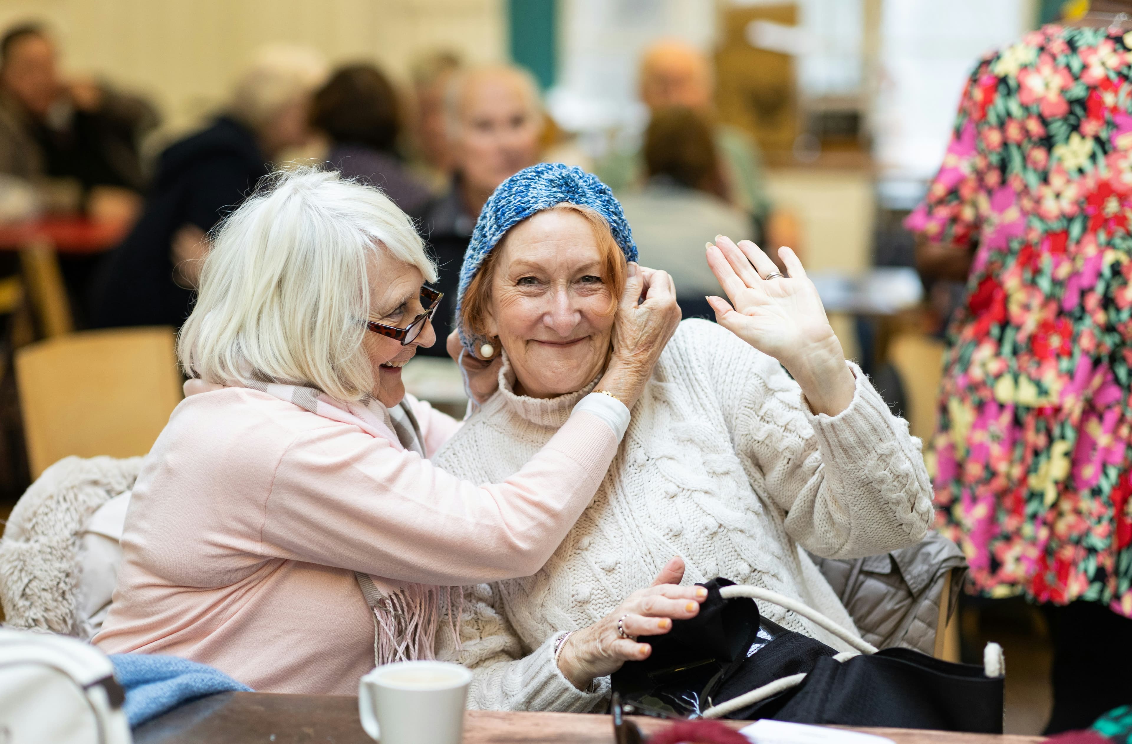 Two older friends laughing as one straightens the other's hat.