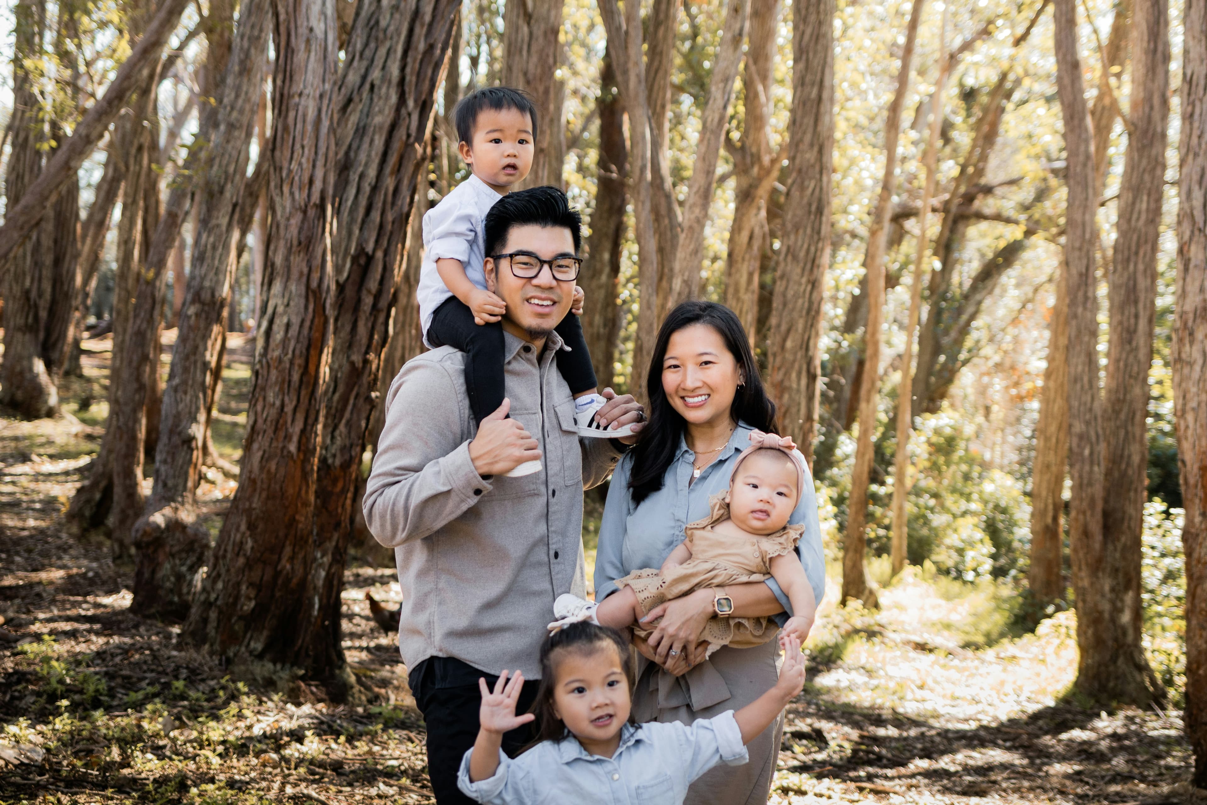 A mother and father with their three young children in a sunny forest.