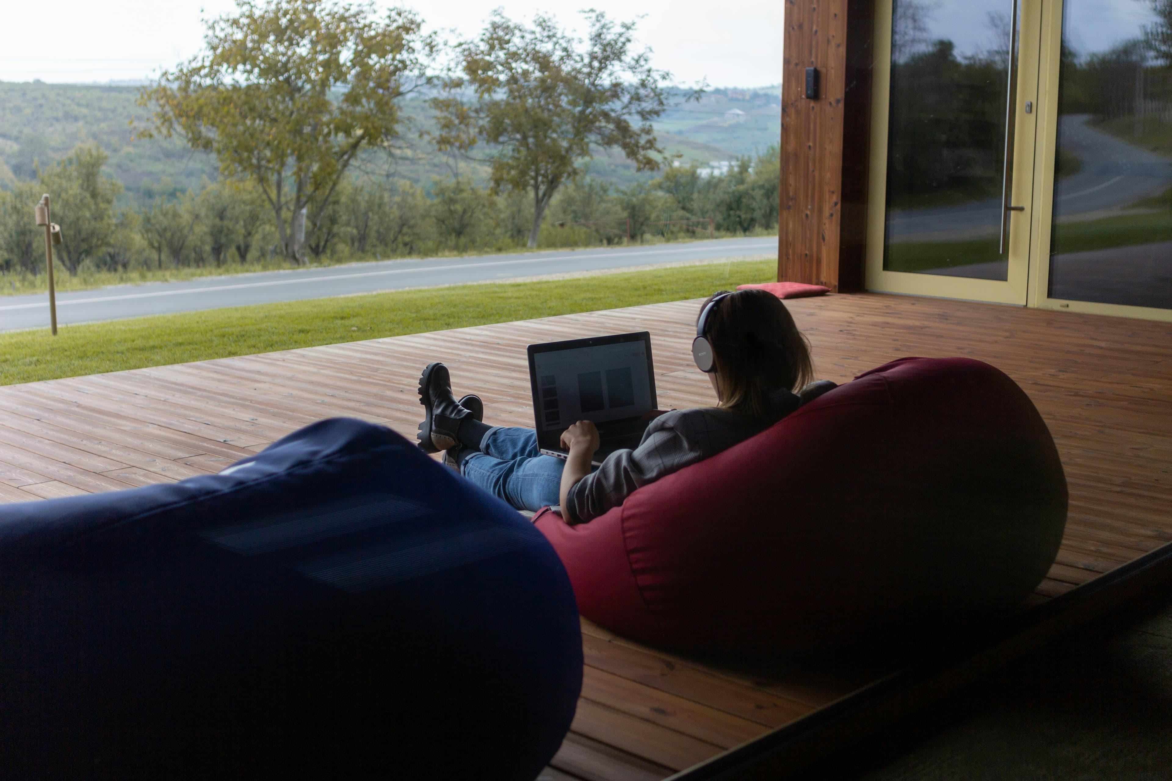 A person in headphones working on a laptop from a beanbag on a porch overlooking the hills.