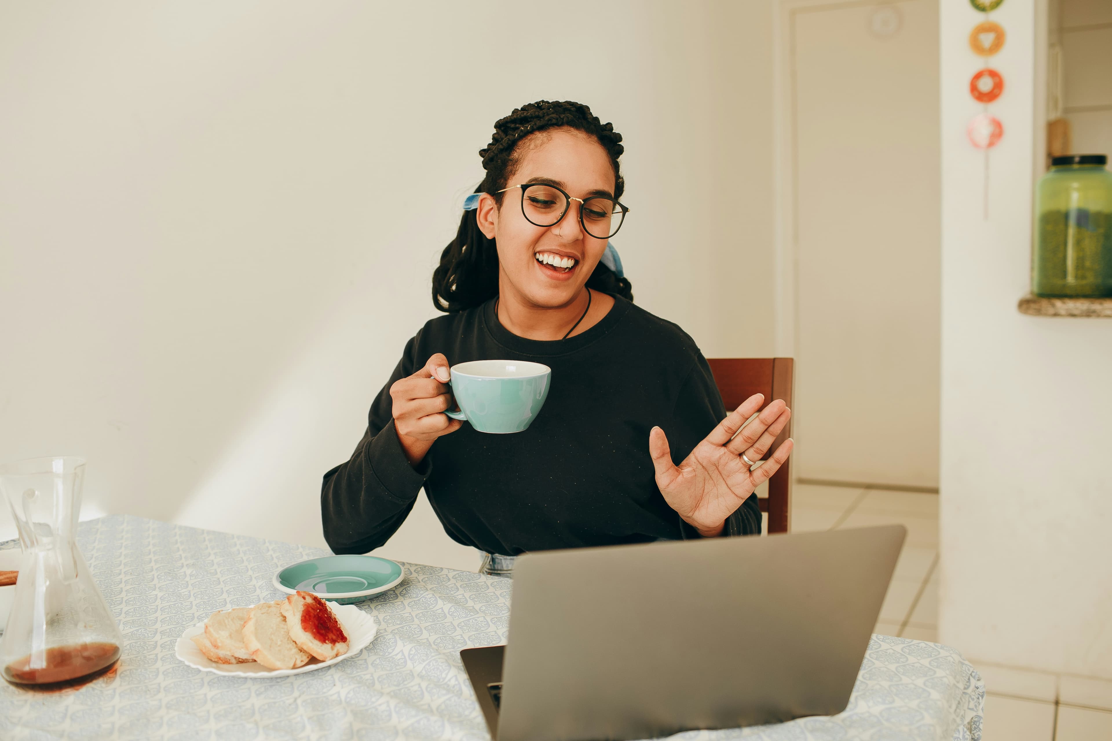 A woman on a video call at her kitchen table, holding a cup of tea.