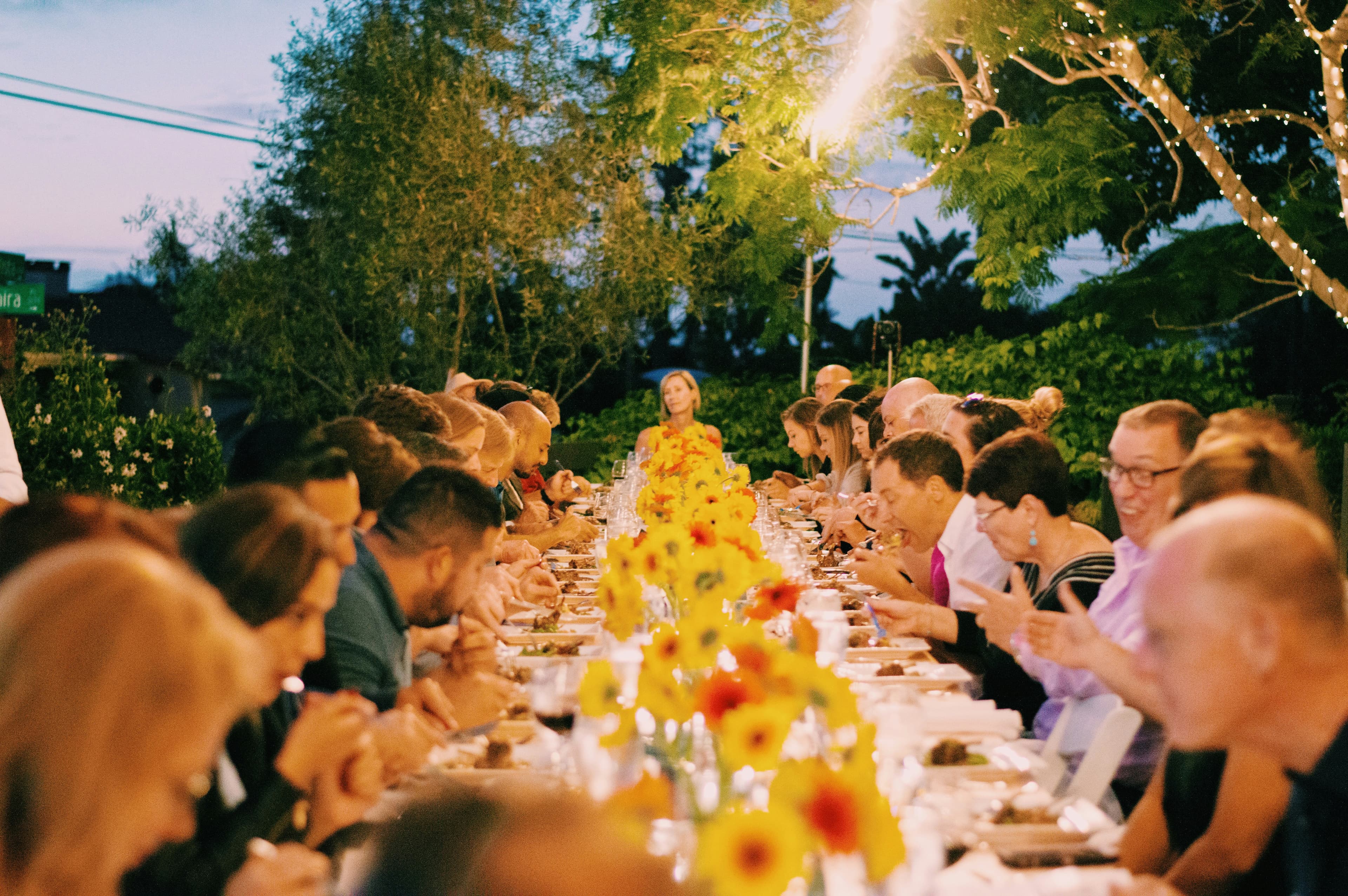 Friends and family at a long outdoor dinner table under string lights.