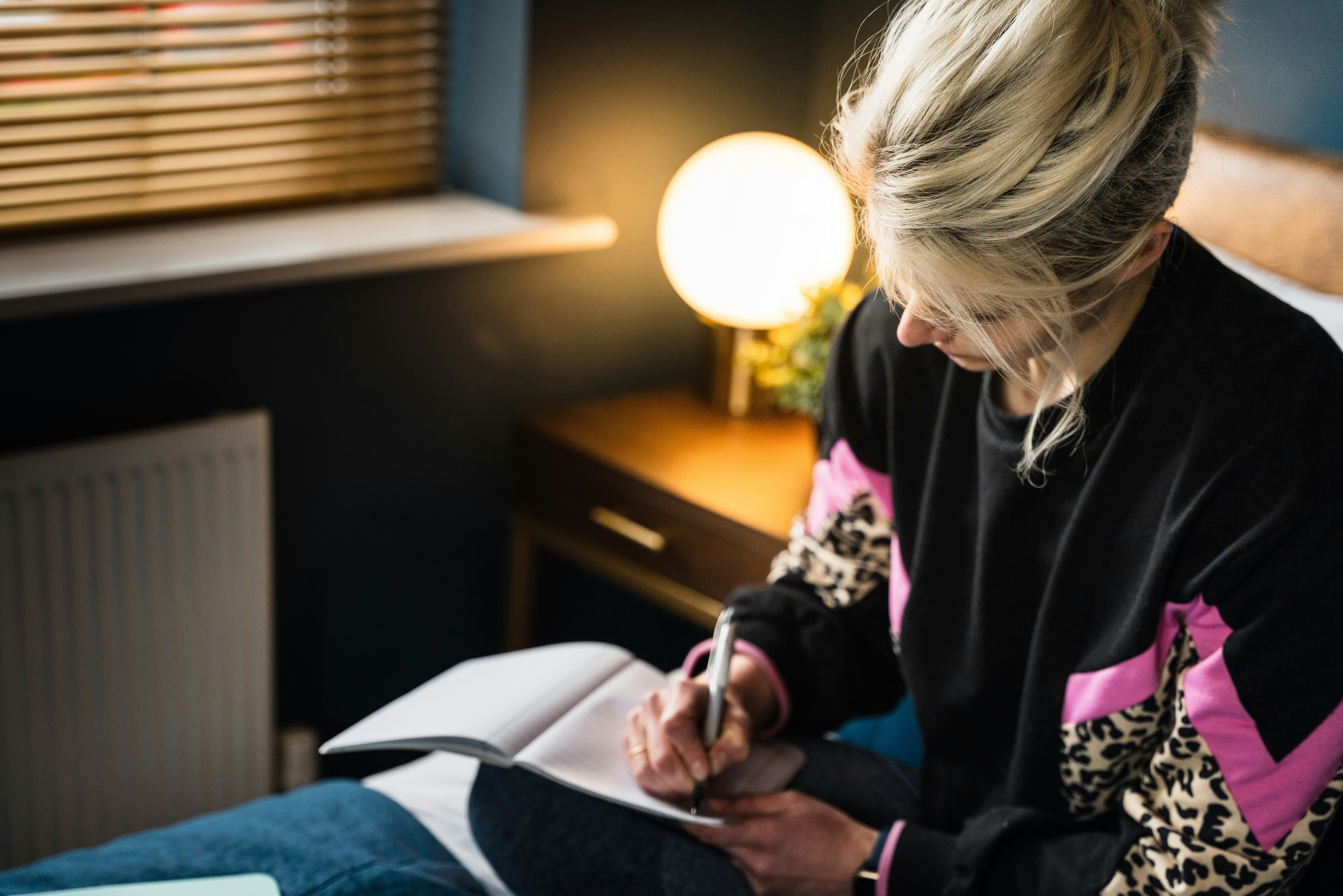 A woman writing in a notebook by lamplight.