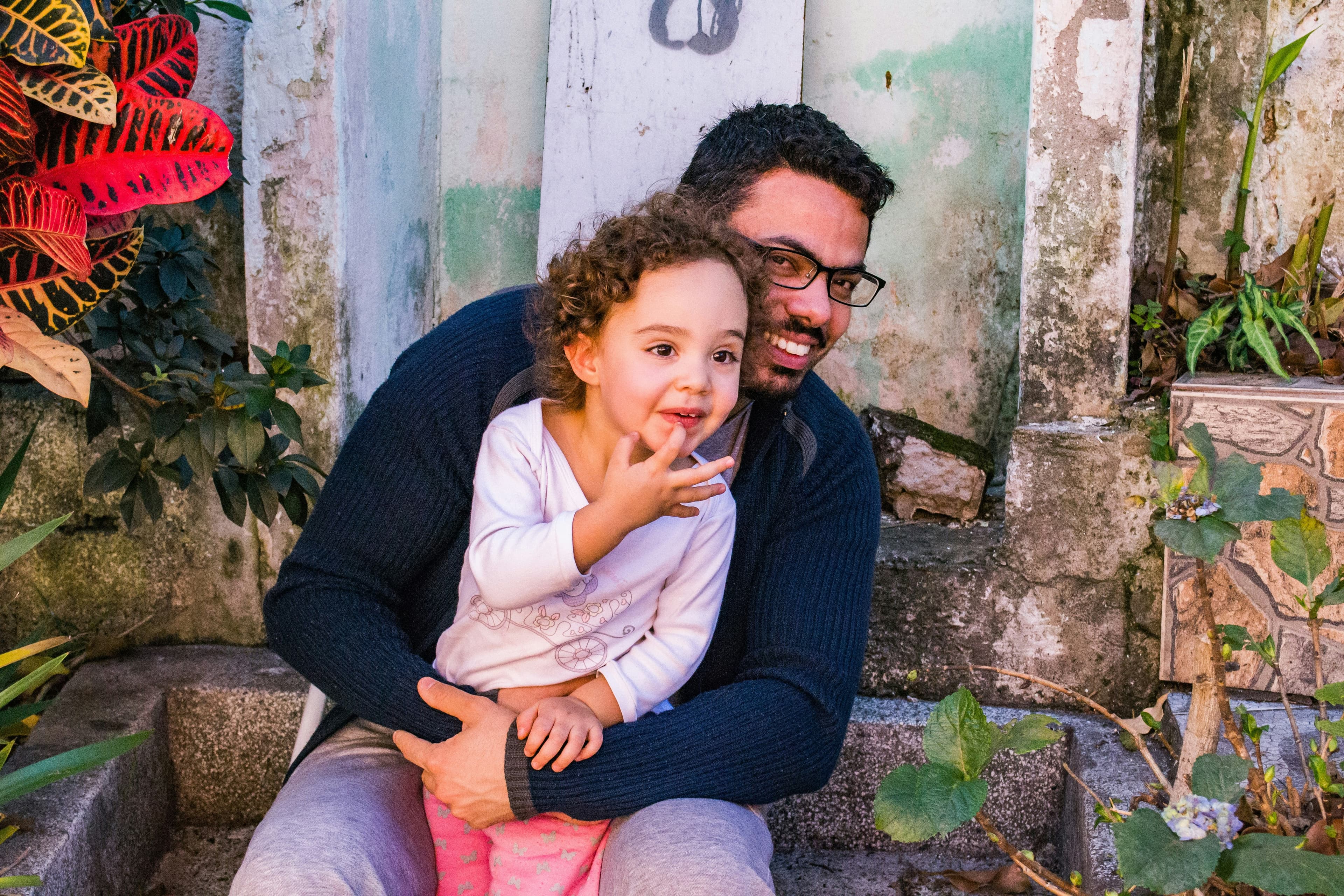 A father hugging his young daughter on the front steps of their home.