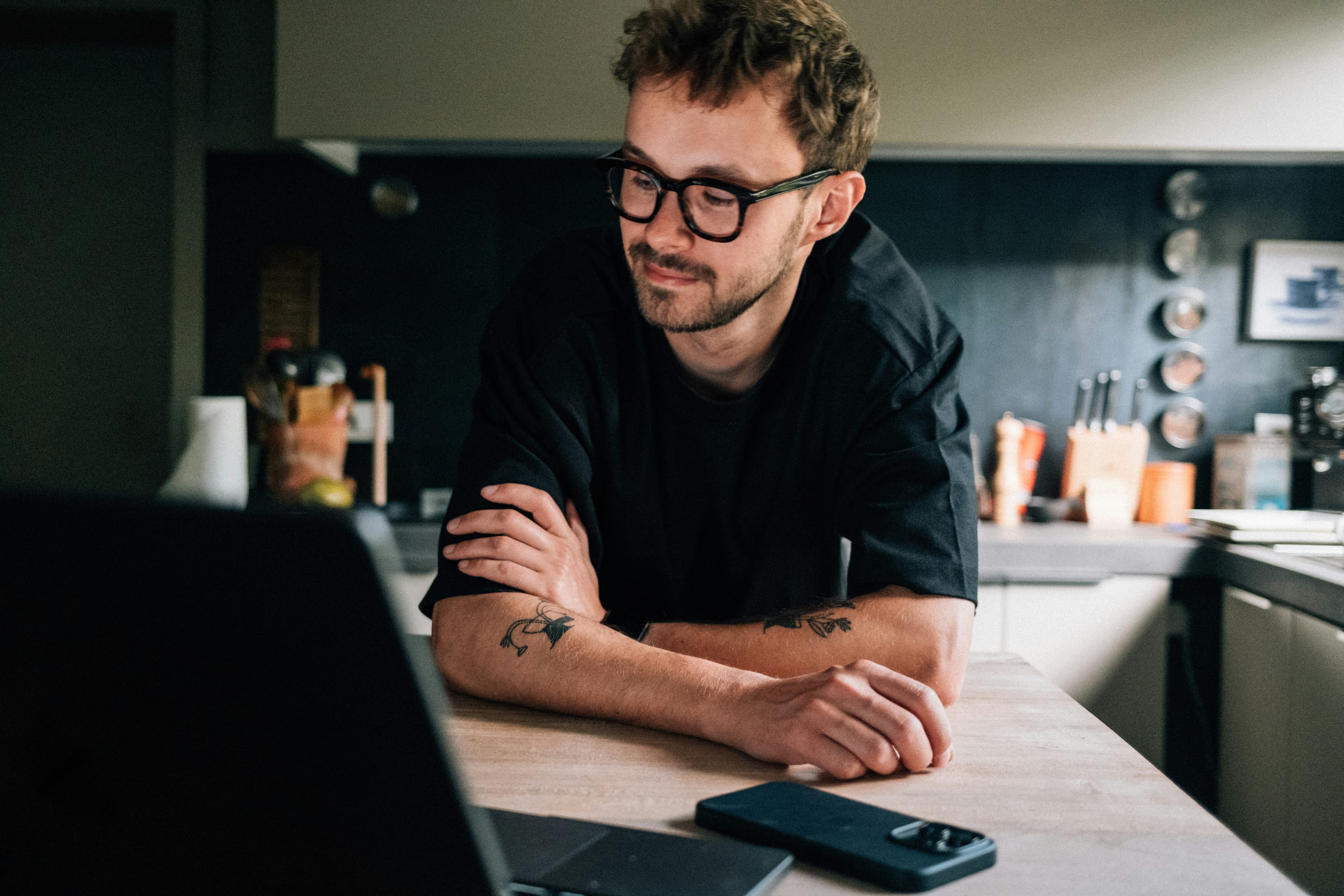 A man smiling at something on a laptop in his kitchen.