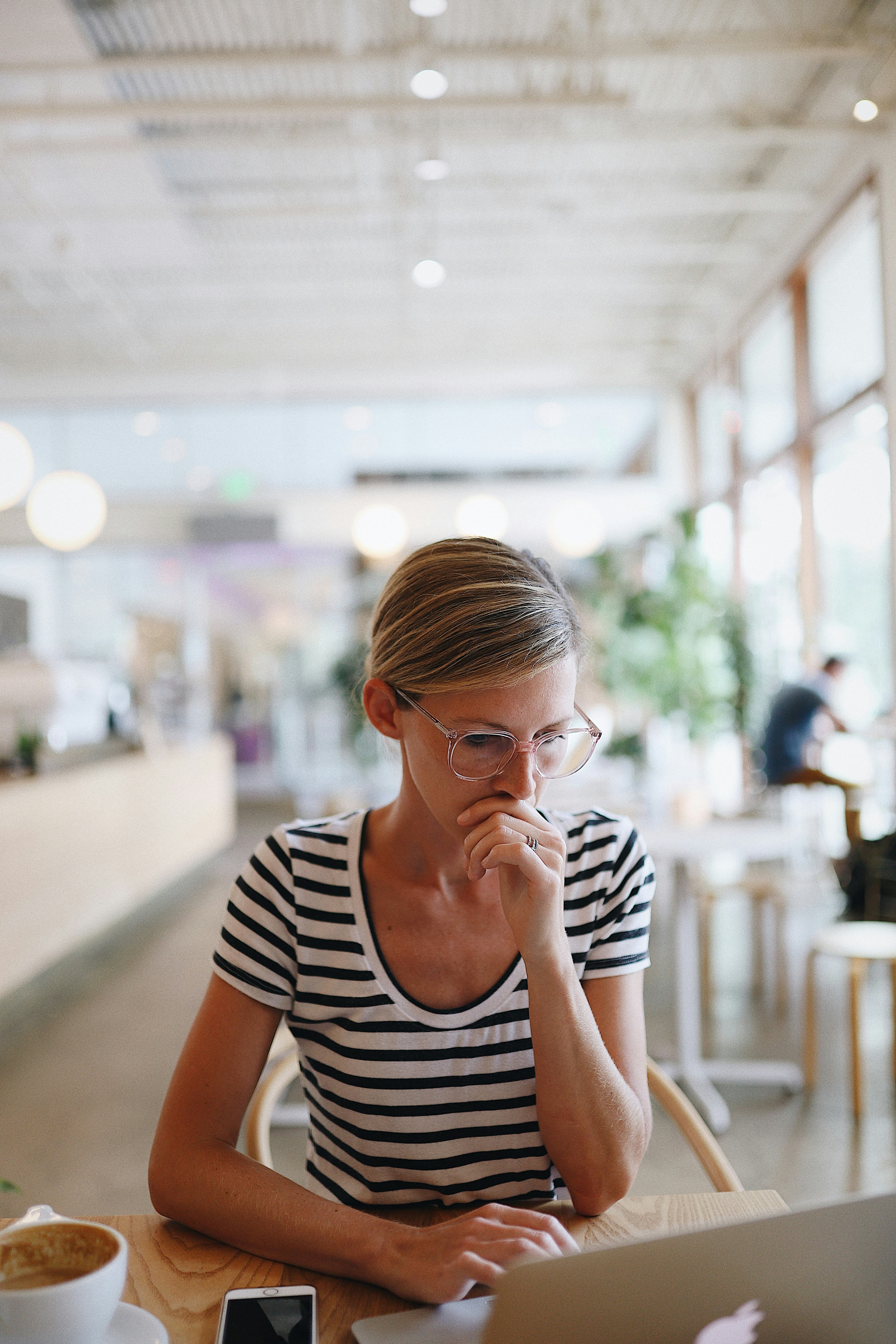 A woman thinking something through at a laptop in a cafe.