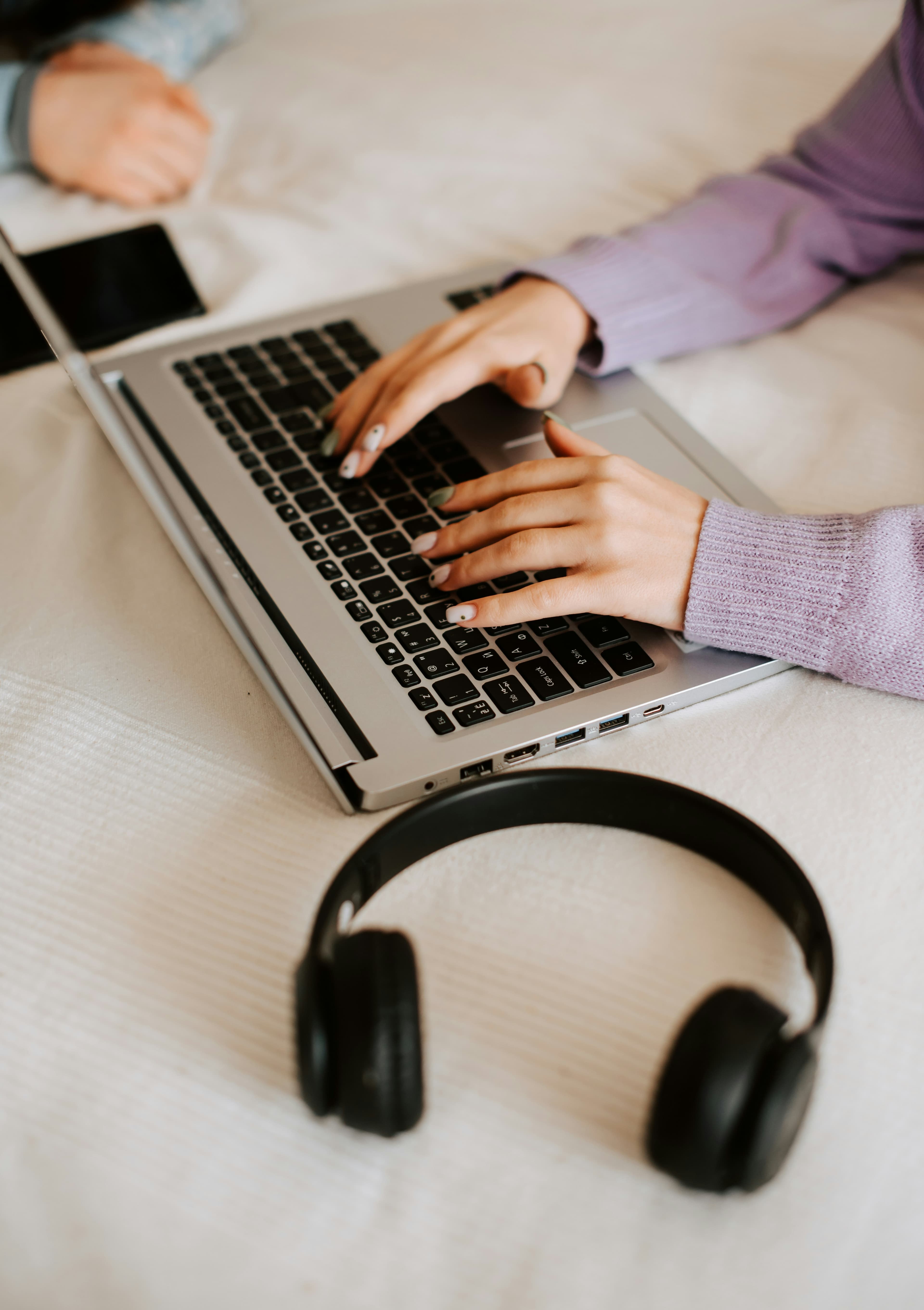 Hands typing on a laptop resting on a bed.