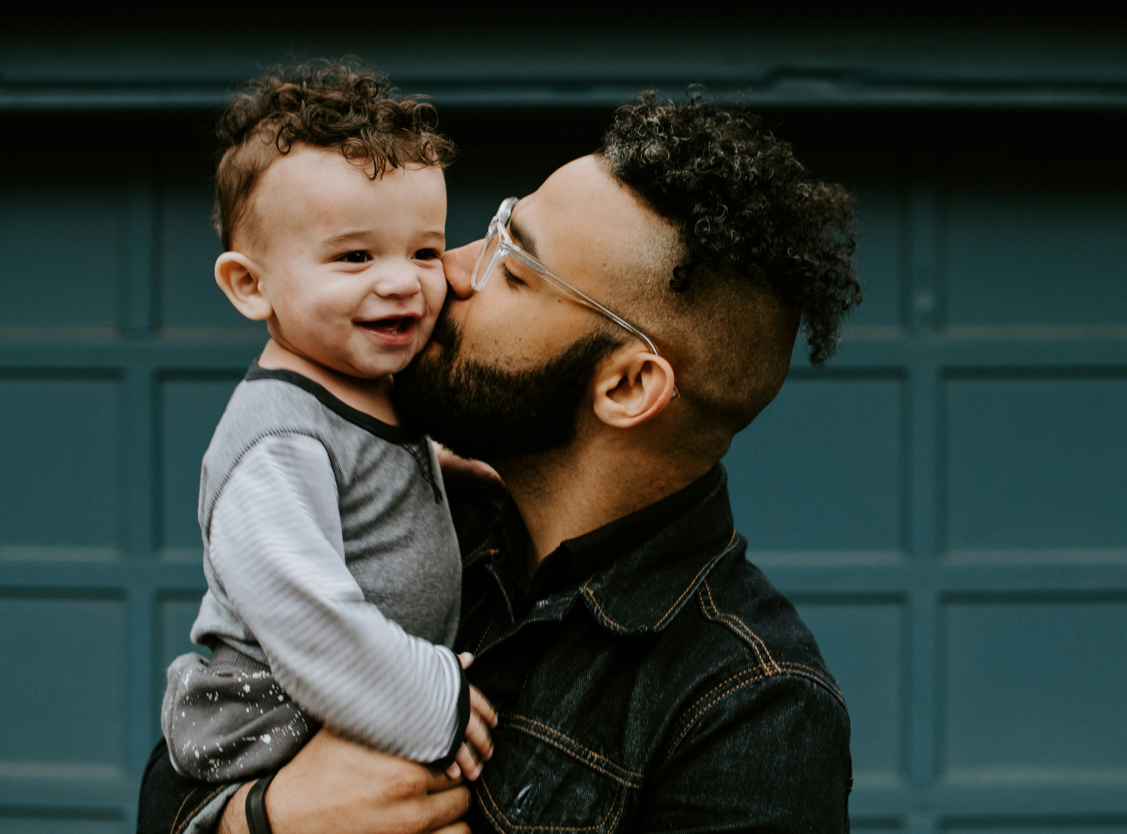 A father kissing his laughing toddler on the cheek.