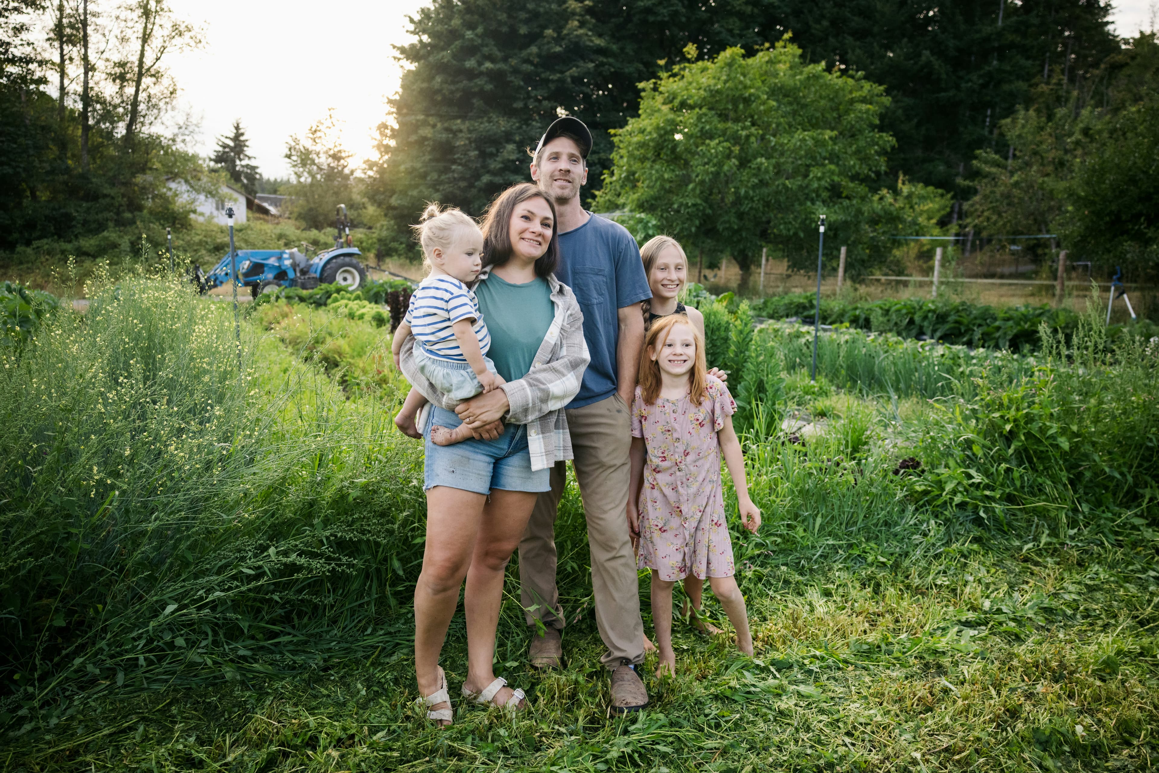 A family of five standing together in their farm's vegetable field.