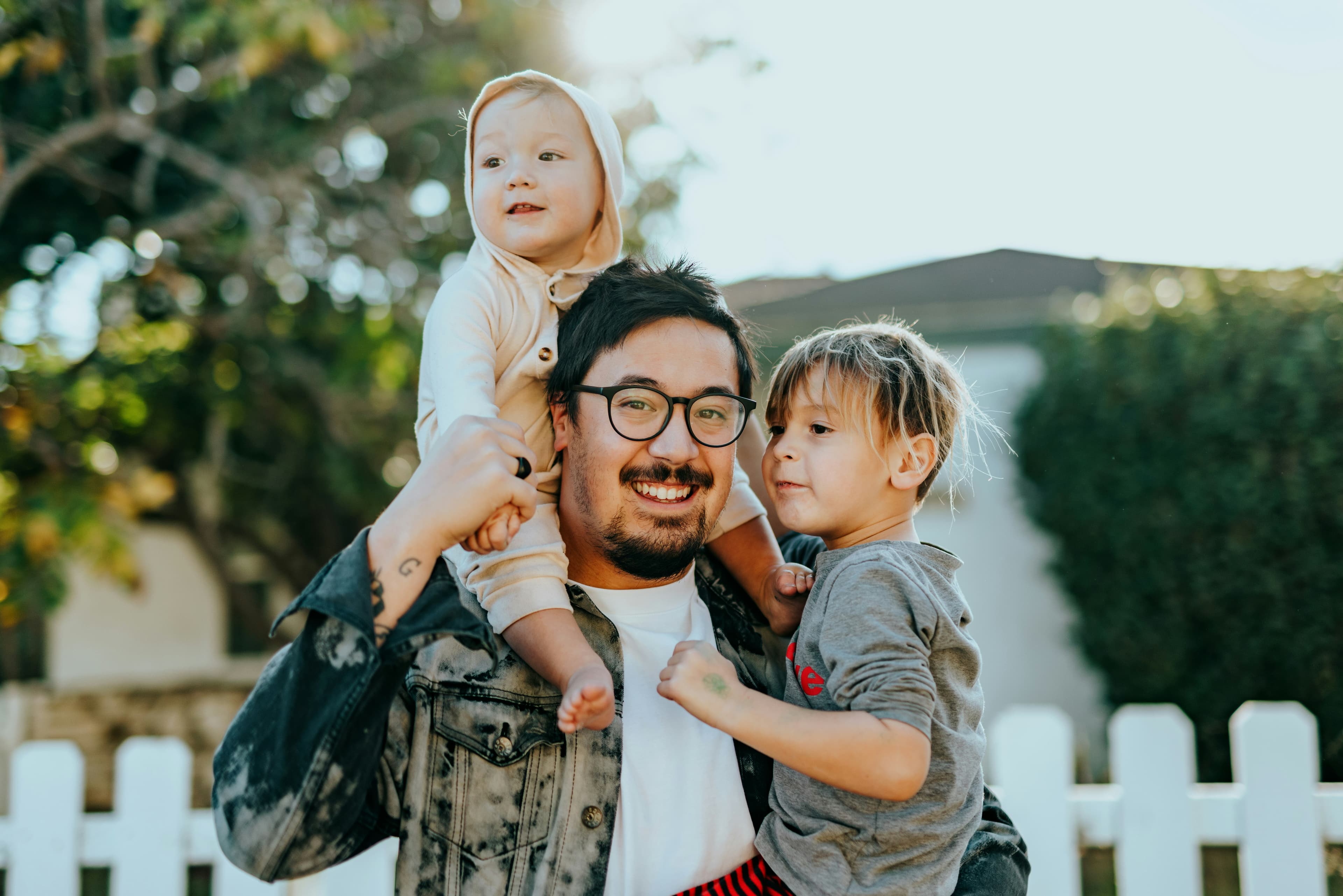 A father smiling with his two young sons in front of their home.