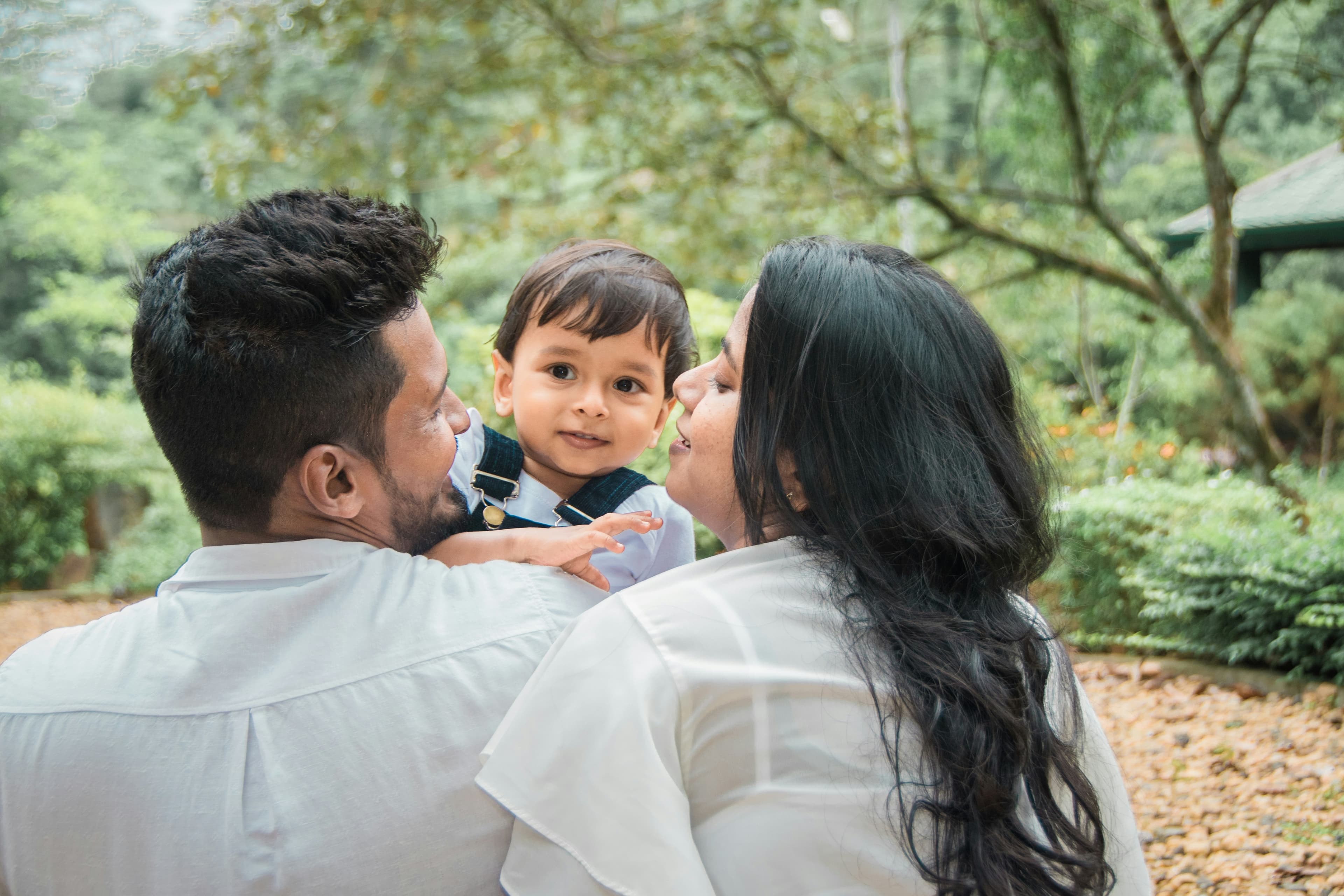 Two parents holding their toddler between them in a garden.