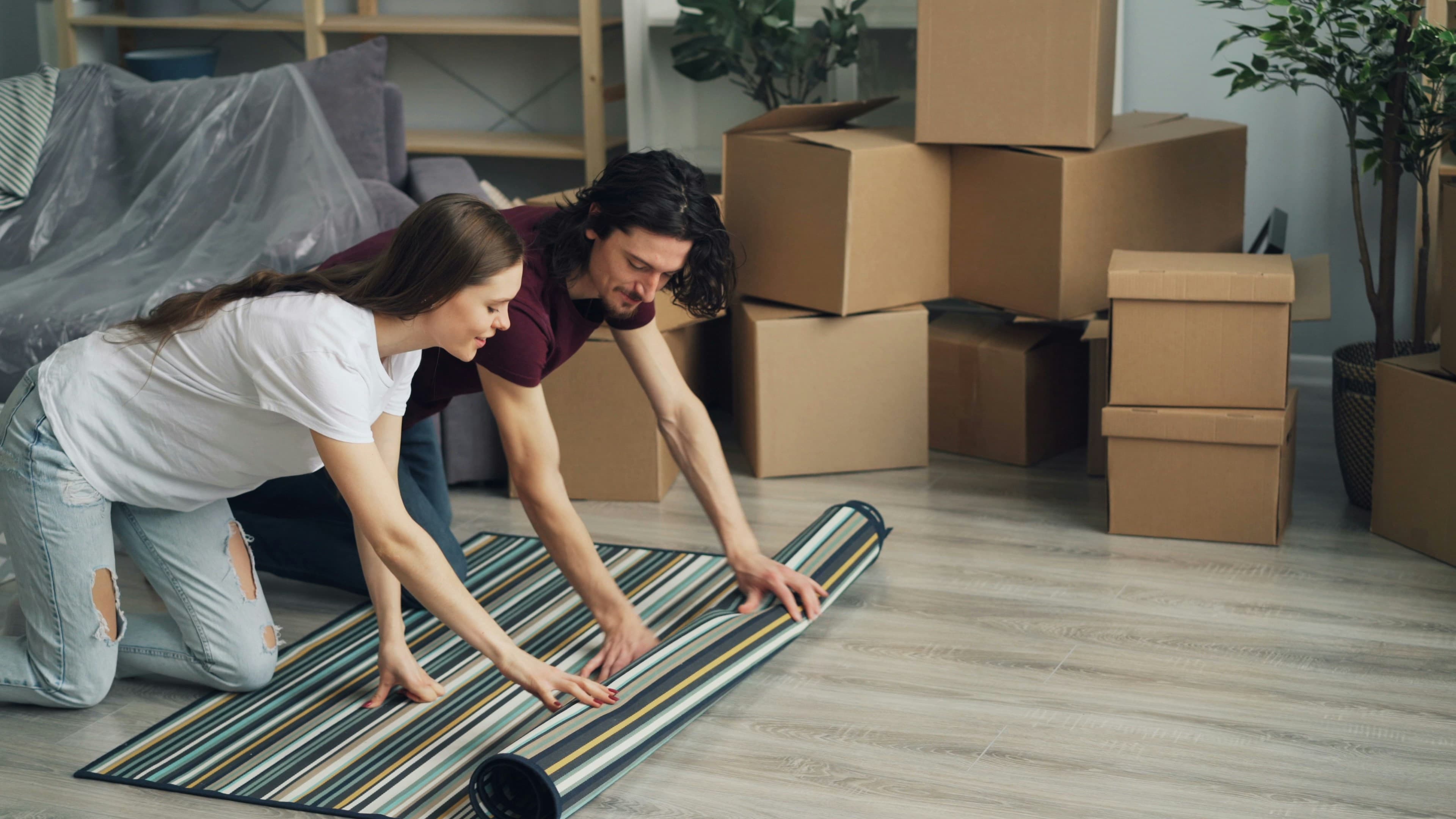 A couple unrolling a rug among moving boxes in their new home.