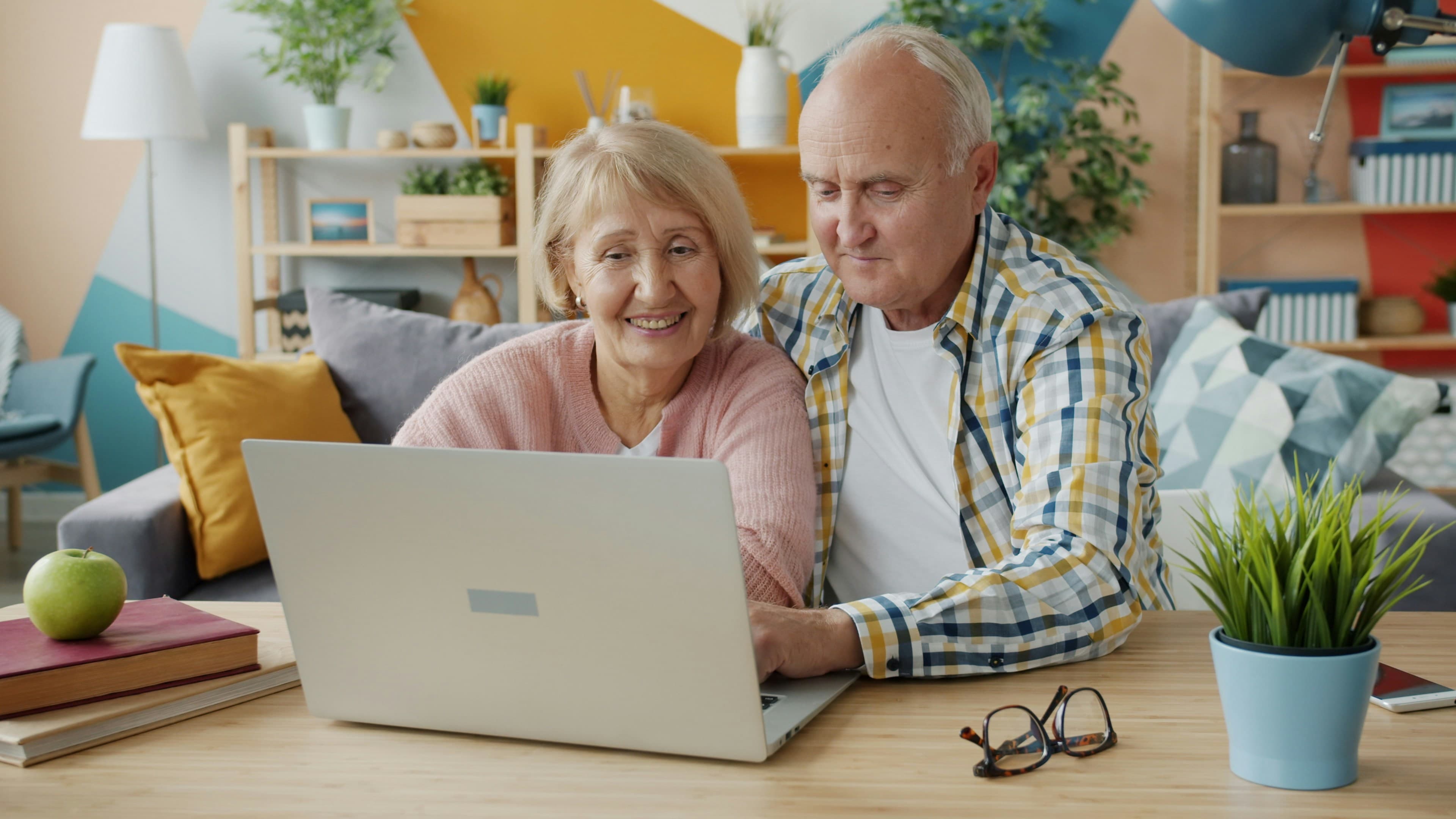 An older couple smiling at a laptop together at home.