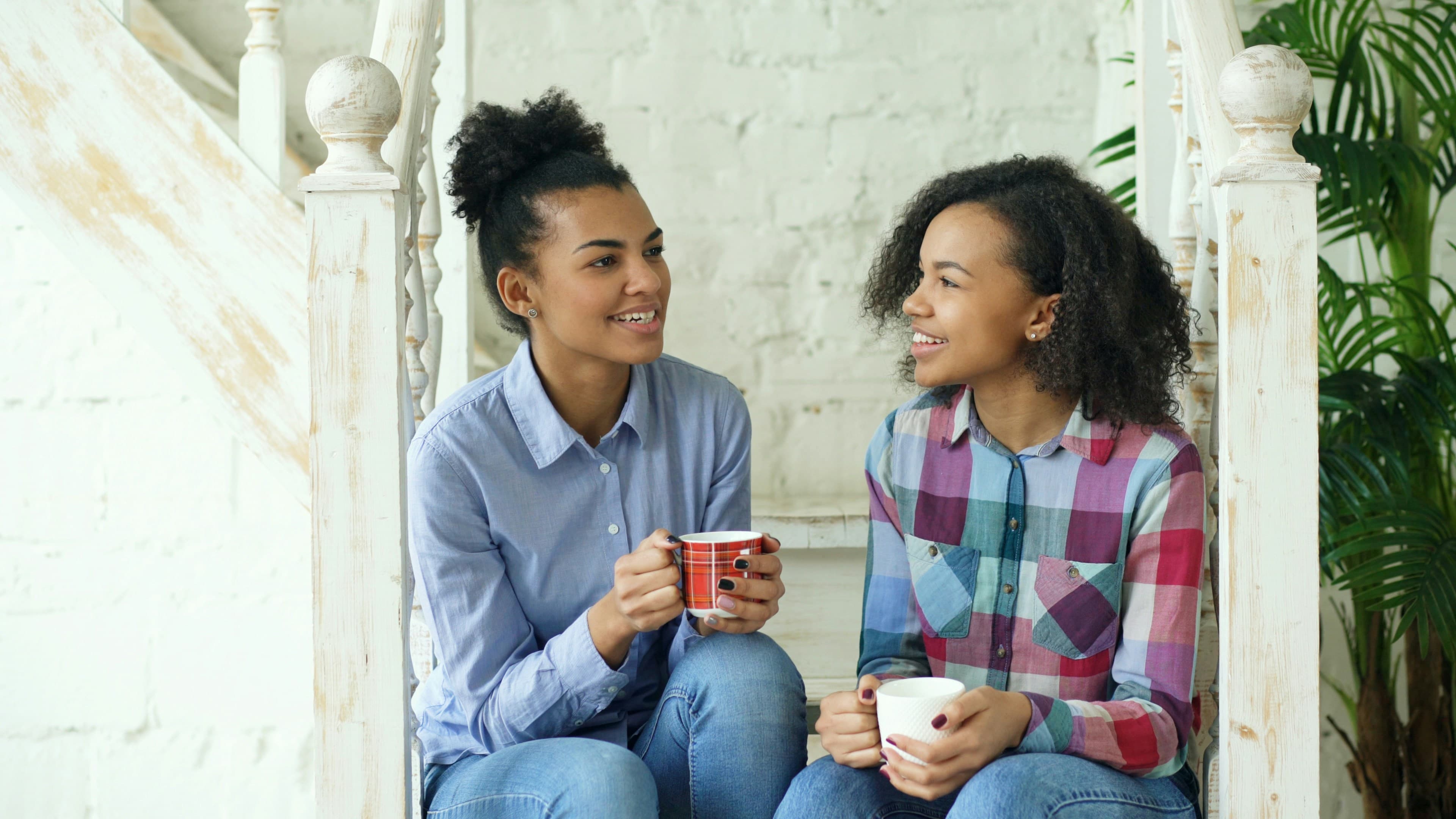 Two sisters talking over coffee on a staircase.