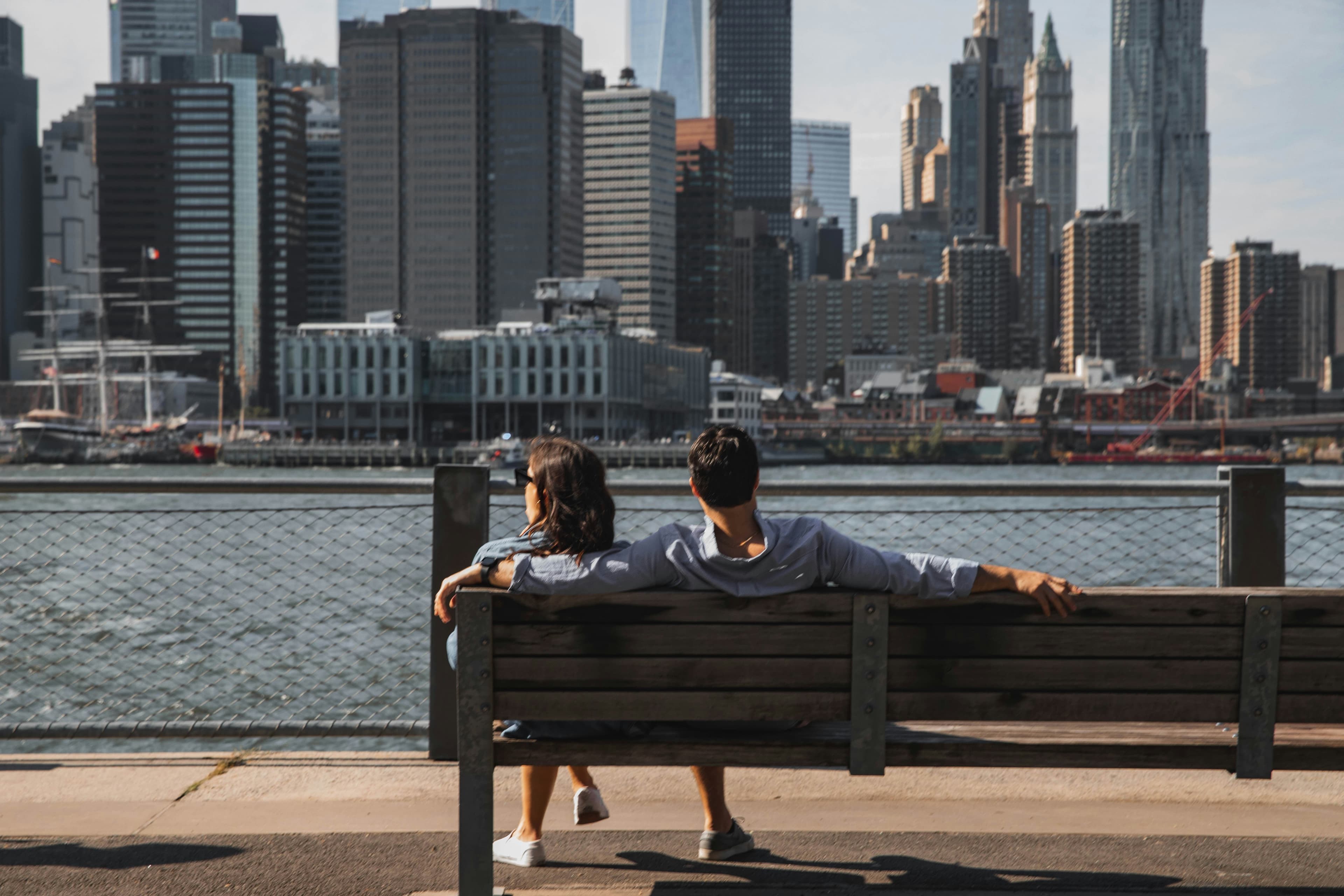 A couple on a waterfront bench looking out at the Manhattan skyline.